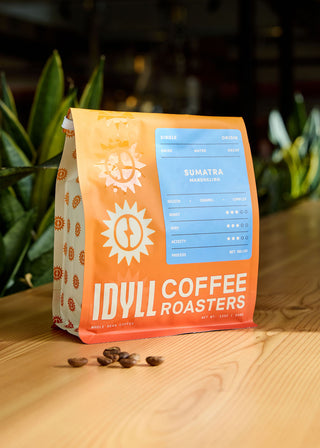 Decaf Sumatra Mandheling coffee bag on a wooden table with a blue label and scattered coffee beans.