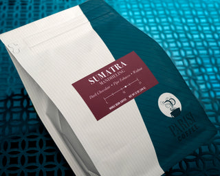 Sumatra Mandheling coffee bag with maroon label beside a white notebook on a teal background