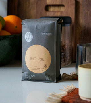 Owl's Howl whole bean coffee bag on a white countertop beside a fruit bowl
