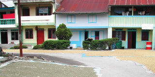 Colorful row of Indonesian houses with blue window frames and laundry hanging on balconies along a sunlit street.