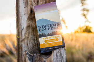 Black Butte Gold coffee bag attached to a weathered wooden post at sunset.