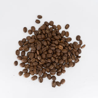 Roasted coffee beans scattered on a white surface with a Topeca bag edge