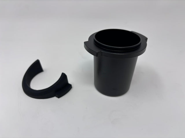 Black single dose grinder body with circular top opening and a detached curved ring nearby.