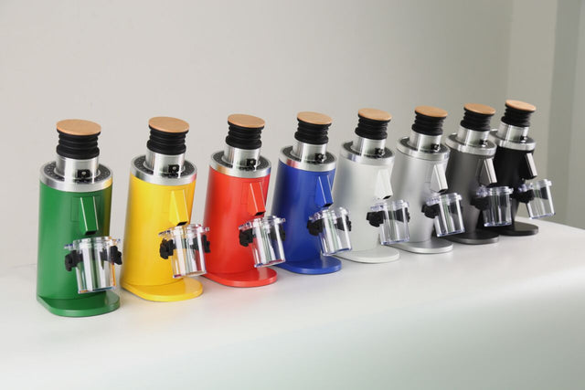 Row of eight colorful Turin DF64 Gen 2.5 single dose coffee grinders on a white surface, each with a wood top.