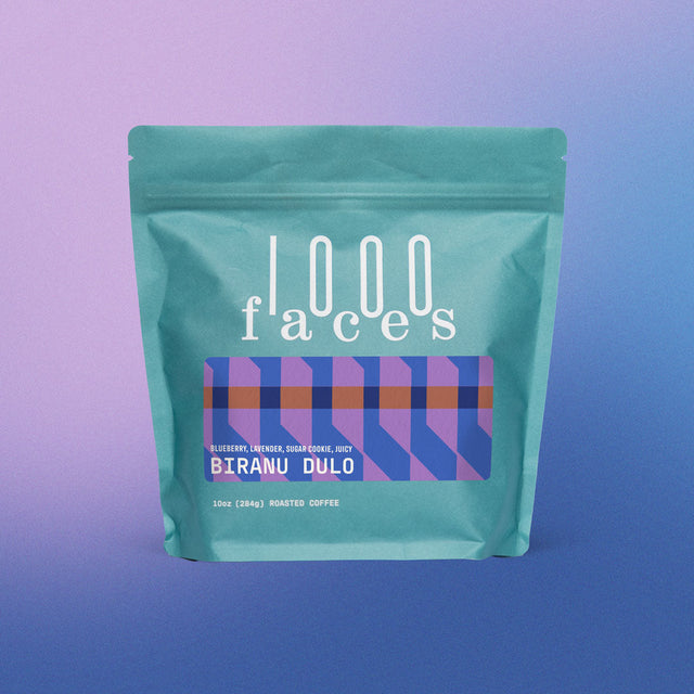 Teal Biranu Dulo coffee bag by 1000 Faces with a purple geometric label against a pink to blue gradient.