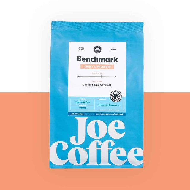 Bright blue Benchmark coffee bag with a white label and large Joe Coffee typography on a peach and white backdrop.