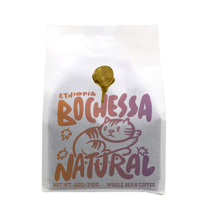 White Ethiopia Bochessa Natural coffee bag with a gold wax seal and a playful cat illustration.