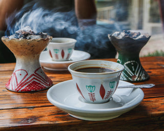 Smoky Ethiopian coffee brewing with a rustic jebena and cups on a wooden table