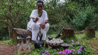 Ethiopian woman in white performs a traditional coffee ceremony outdoors with cups arranged on a tray.