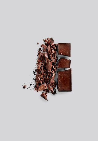 Shards and blocks of dark chocolate on a light gray background representing Ceremony Antithesis espresso flavor notes