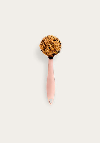 Rose gold spoon filled with brown sugar crystals on a pale background