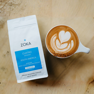 Zoka Cuatro espresso bag beside a latte with latte art on a wooden surface