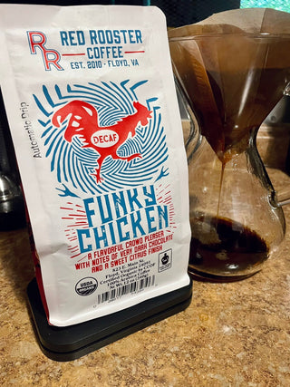 Red Rooster Funky Chicken Decaf bag on the counter beside a glass coffee carafe