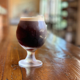 Dark stout in a stemmed glass with a foamy tan head on a wooden bar