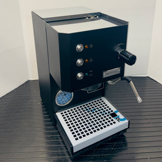Open box Profitec GO with the machine partially exposed showing front gauges and a portafilter attached.