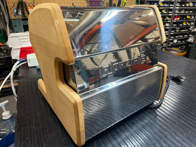 Close up of a shiny chrome LUCCA espresso machine with maple wood side panels on a workshop bench