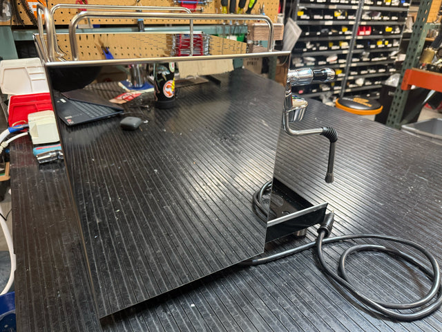 Close up of a chrome ECM Classika espresso machine component with a curved portafilter handle on a workbench