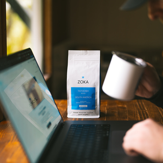 Zoka Tatoosh dark roast coffee bag on a wooden table beside a laptop