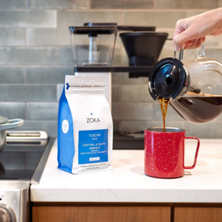Zoka Tuscan coffee bag on a kitchen counter as coffee pours into a speckled red mug