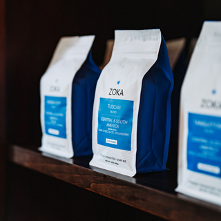 Zoka Tuscan blend coffee bags arranged on a shelf with a prominent blue labeled bag in the foreground