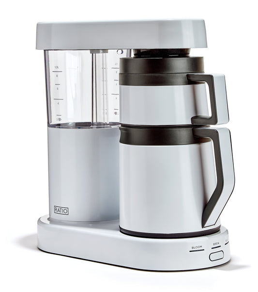 Side close up of Ratio Six White espresso machine showing transparent water reservoir with measurement marks and logo at the base.